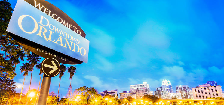 A sign reading Welcome to Downtown Orlando with the skyline of the city in the background
