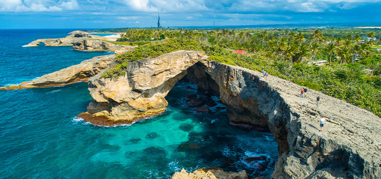 Stunning aerial view of a natural rock arch along a Caribbean coastline, with lush greenery, turquoise waters, and a sense of adventure—perfect for budget-conscious travelers seeking hidden gems.