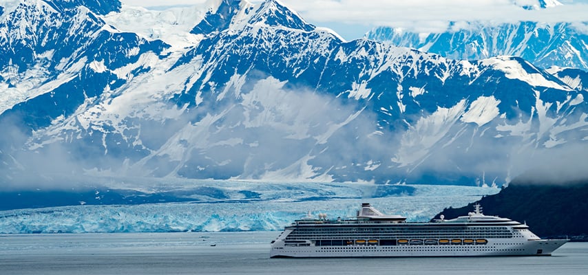 Cruise ship sailing past glacier and snow-capped mountains in Alaska