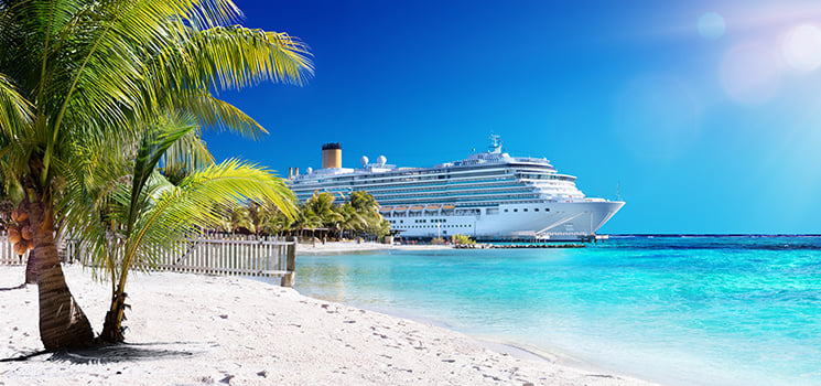 A picturesque Caribbean cruise scene showcases a stunning white-sand beach, swaying palm trees, and a massive cruise ship anchored offshore in the crystal-clear turquoise waters.