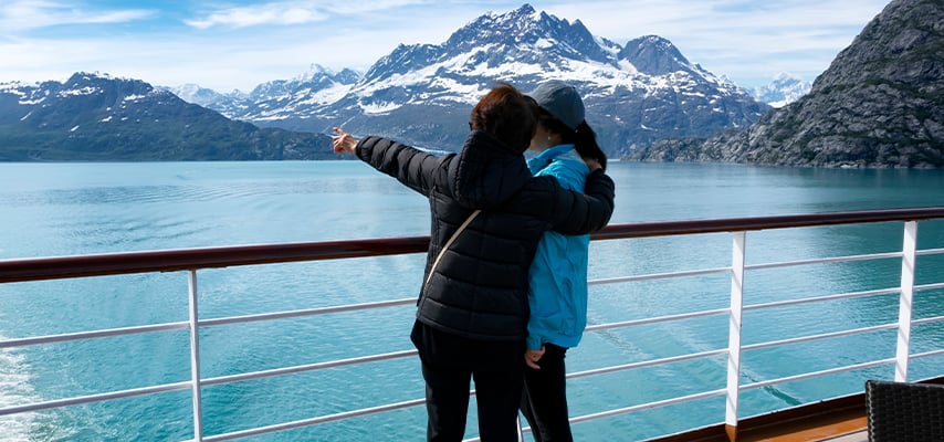Mother holding her daughter while pointing to mountains and glaciers in Alaska while on ship