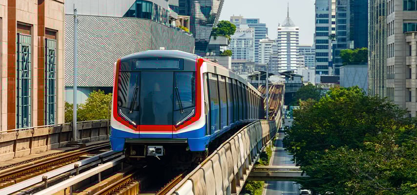 Skytrain on tracks through green urban Bangkok landscape with buildings.