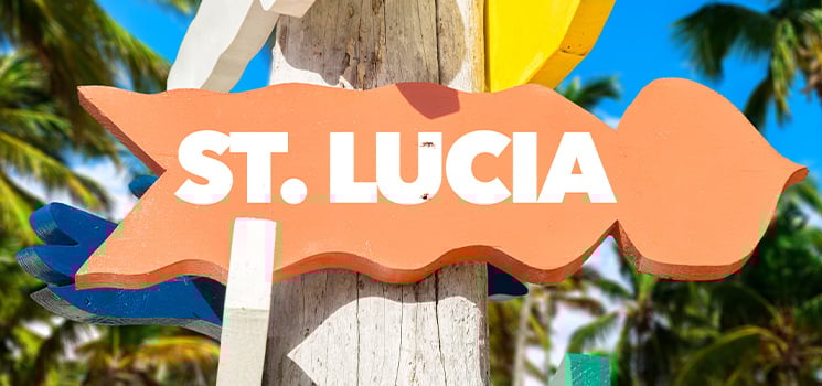 A vibrant directional sign points the way to the lush Caribbean island of St. Lucia, surrounded by swaying palm trees against a brilliant blue sky.