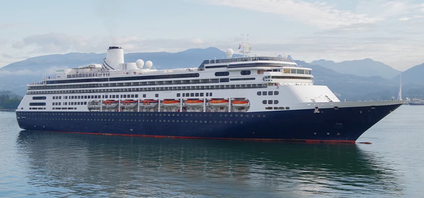 Large cruise ship with dark hull and white superstructure sailing past mountainous coastline.
