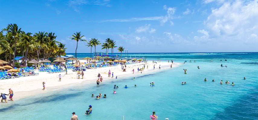Winter in Puerto Rico beach scene with turquoise water, people swimming, and lounging under palm trees on a sandy shore.