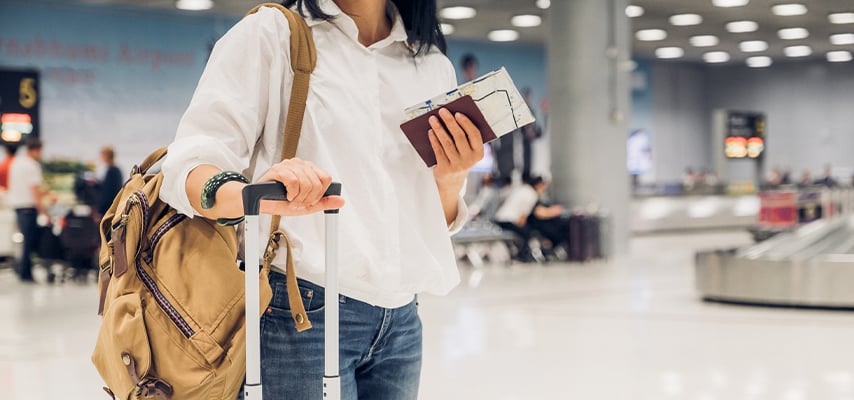 Woman backpacker holding passport and map with suitcase standing at check in baggage at airport terminal