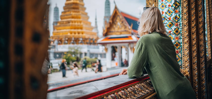 Tourist in green shirt admiring golden temple spires and decorated buildings at Thai palace complex.