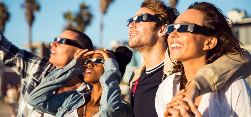 Group of people wearing eclipse safety glasses looking up at sky during solar eclipse viewing event.