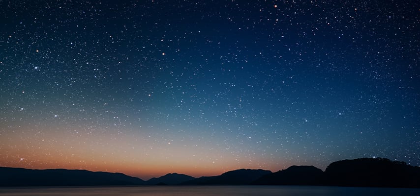 A movement of stars in the night sky with the view of mountains