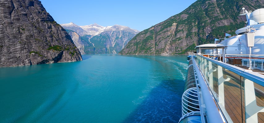 View from cruise ship deck of turquoise fjord waters surrounded by towering mountain cliffs.