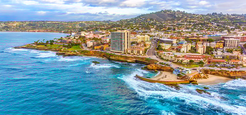 Aerial view of coastal town with turquoise ocean, rocky shoreline, and buildings on hillside