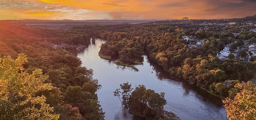 Aerial sunset view of winding river through dense forest with small island
