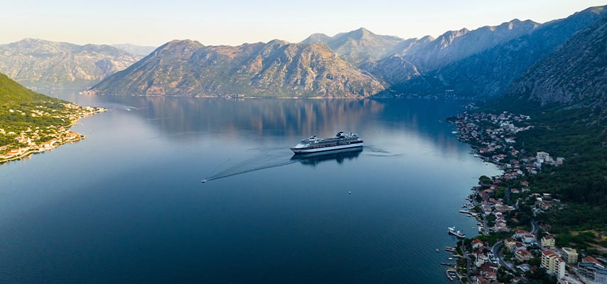 Aerial view of cruise ship in deep blue fjord surrounded by mountainous Alaskan coastline.