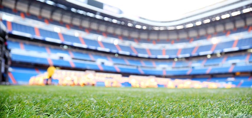 Blurred view of Santiago Bernabéu Stadium's blue and red seating tiers from field level, with soft lights glowing in the stands.