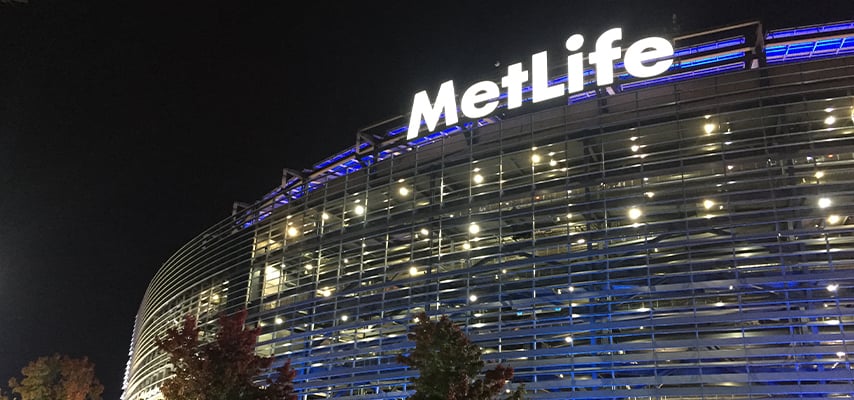MetLife Stadium exterior at night showing illuminated corporate signage and distinctive modern facade design.
