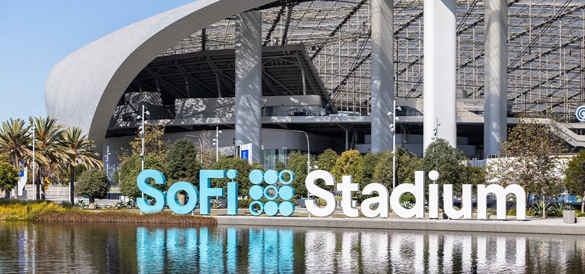 SoFi Stadium's modern curved architecture with large branded sign visible near palm trees and water feature.