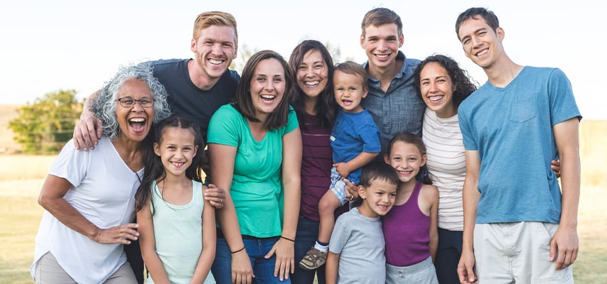 Happy extended family with children and adults of all ages smiles together in sunny park.