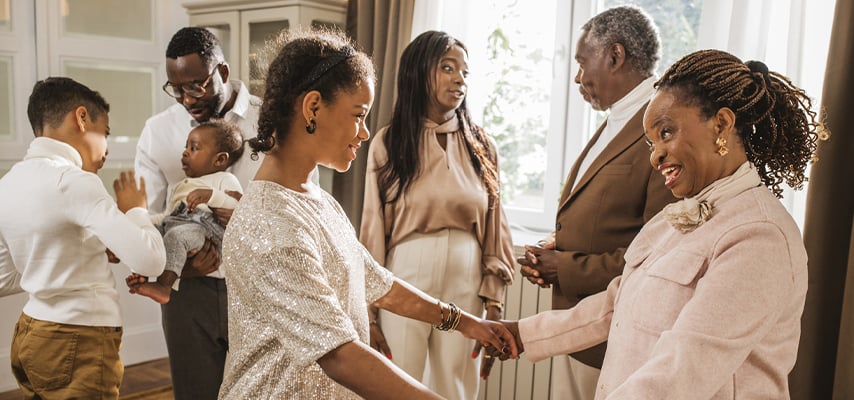 Well-dressed family members greet and embrace in elegant home during formal reunion gathering.