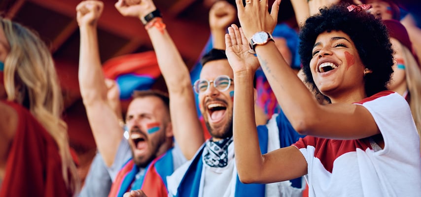 Excited sports fans with painted faces cheering and raising their arms in celebration at a stadium.