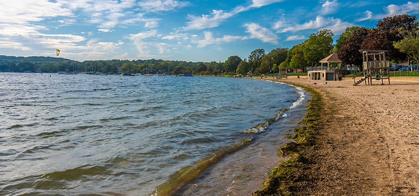 Sandy lakeside beach along calm lake with playground and trees under blue sky