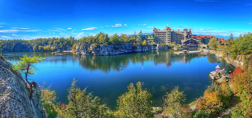 Panoramic view of grand hotel on cliff overlooking still lake with blue sky