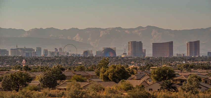 Distant view of the Las Vegas skyline from a residential neighborhood, with the Sphere and High Roller Ferris wheel visible among the city's buildings and desert mountains.