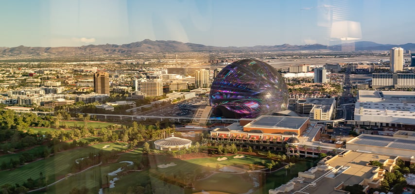 Aerial view of the Sphere entertainment venue in Las Vegas displaying a vivid multicolor LED exterior, surrounded by the city and desert landscape.