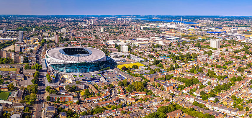 Aerial view of Tottenham Hotspur Stadium in London, surrounded by dense residential neighborhoods stretching toward the horizon.