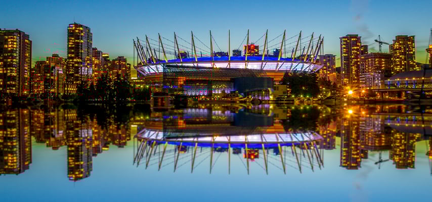 BC Place Stadium in Vancouver illuminated at night with city skyline reflected in water during twilight hours.