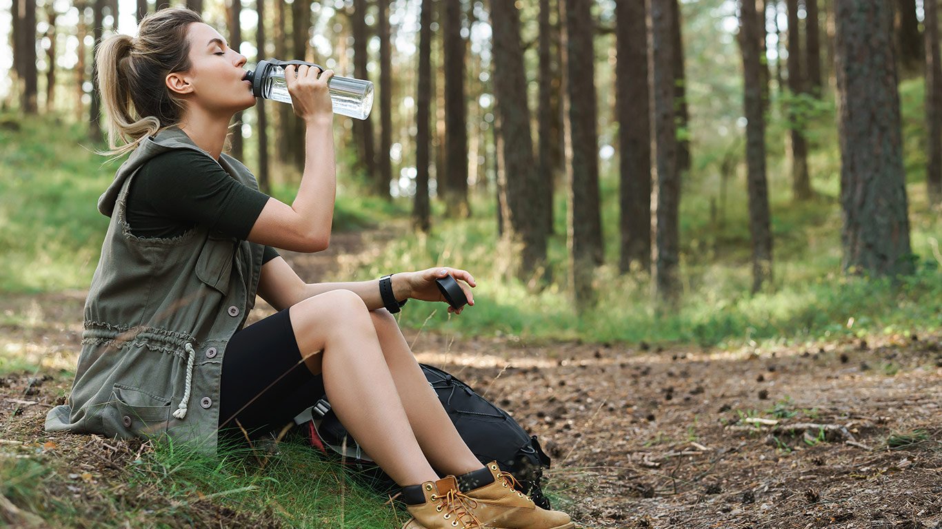 person using refillable water bottle while hiking in the woods