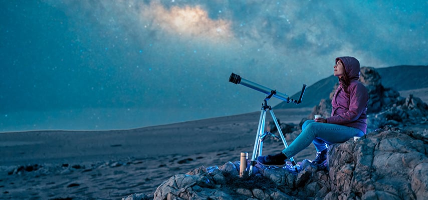 Woman sitting in the desert looking at the starry sky and the milky way in the background