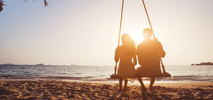 romantic couple in love sitting together on rope swing at sunset beach