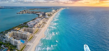 Panoramic aerial view of Cancun's hotel zone with pristine beaches, turquoise Caribbean Sea, and a boat cruising along the coastline at sunset.