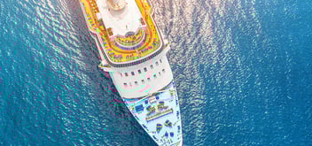 Nose of a cruise ship in a turquoise sea, with a glare from the sun on the water.