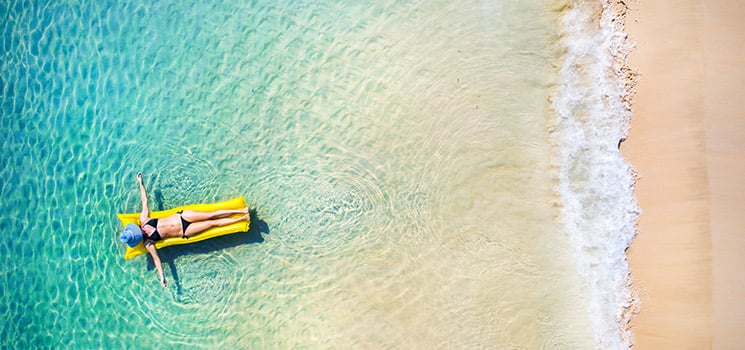 Young woman in hat relaxing on the yellow air mattress in tropical sea