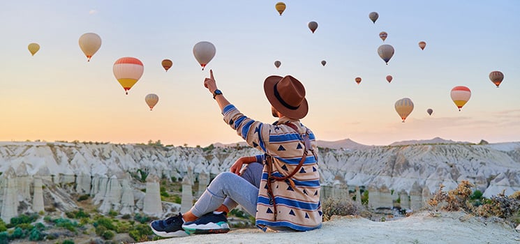 Person in hat and patterned sweater watching hot air balloons over Turkey.