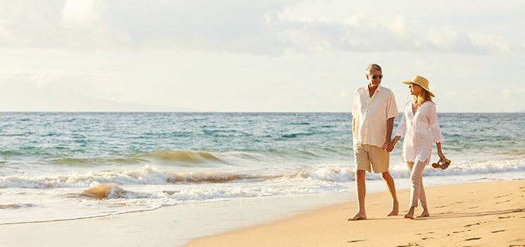 Mature couple walking on the beach at aunset
